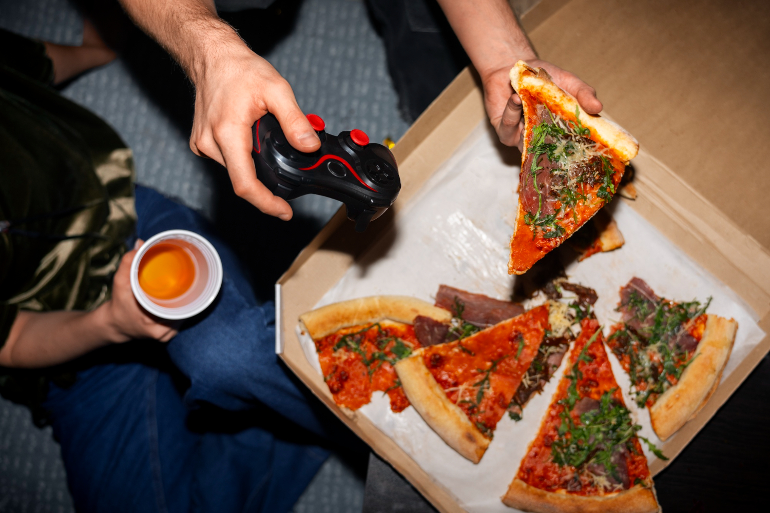 A person having food and a gaming console in one hand