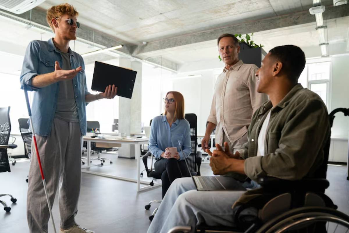 A diverse group of professionals engaged in a meeting, with one person presenting using a laptop in a modern office setting.