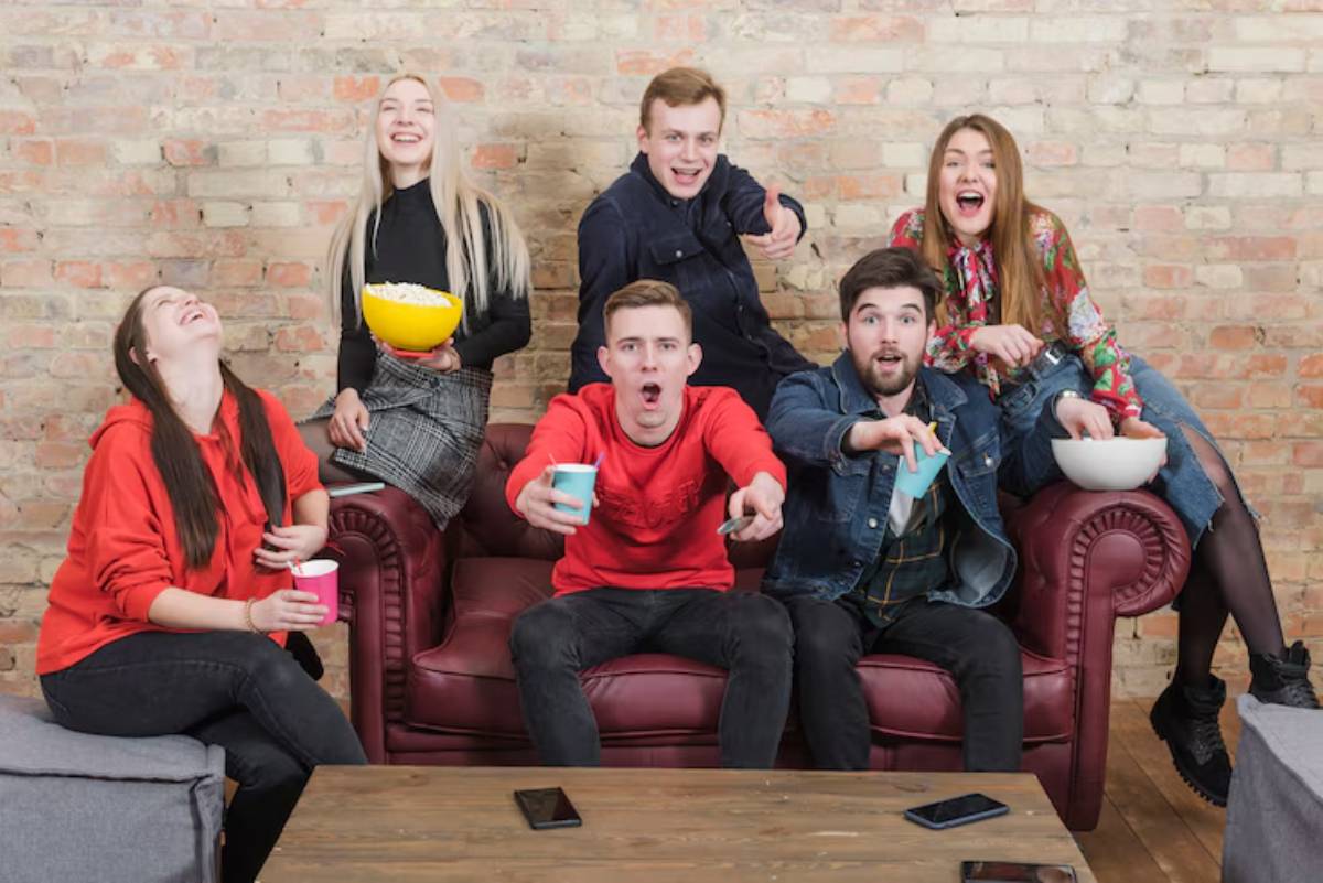 A group of friends enjoying snacks and drinks while lounging on a red couch in a cozy, rustic setting.