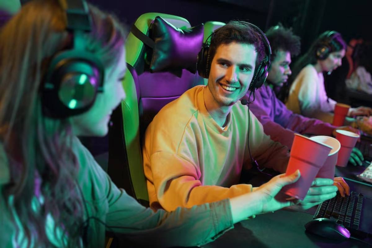 A group of gamers with headsets share drinks in a vibrant gaming environment, illuminated by colorful lights.