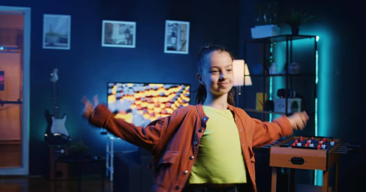 A person stands in a vibrant room, dressed in a green shirt and cozy orange jacket, with arms outstretched, enjoying the moment.