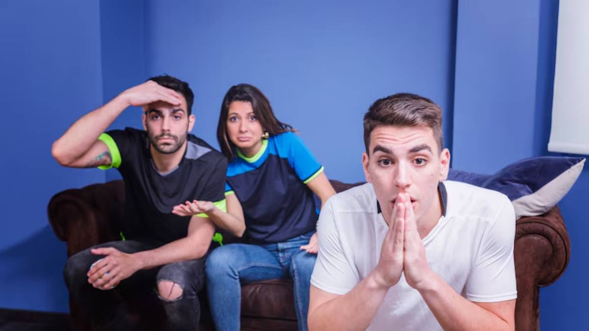 A group of three people on a couch, expressing different emotions, against a bright blue wall background.