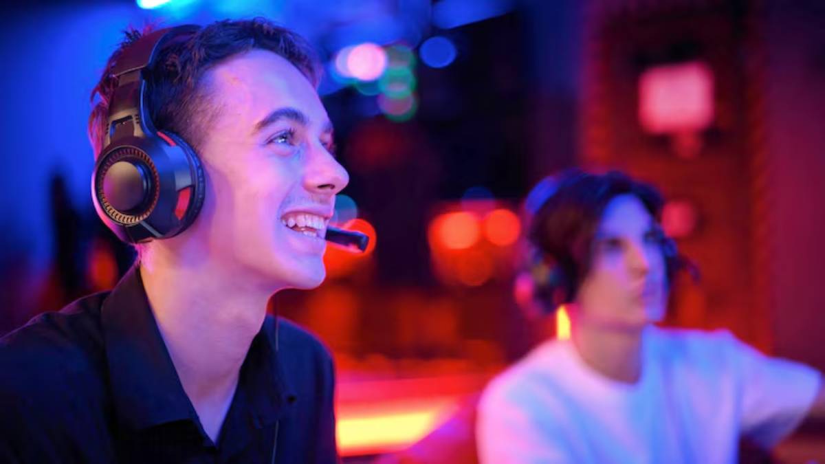 Two individuals wearing gaming headsets are engaged in a vibrant gaming session, illuminated by colorful lights in a modern gaming environment.