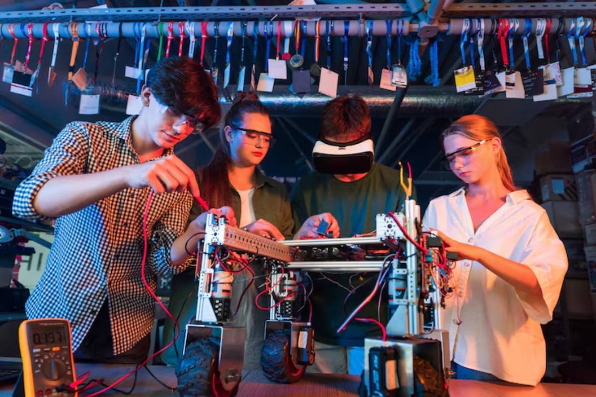 Four people work collaboratively on a robotic device, surrounded by tools and colorful wires in a vibrant workshop environment.
