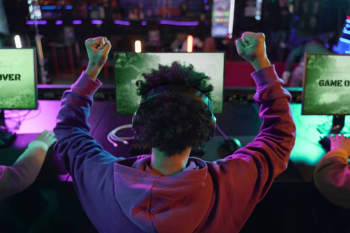 A gamer celebrates with raised fists in a vibrant gaming center, with screens displaying 