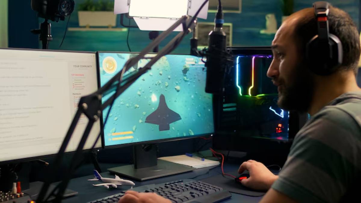 A gamer sits at a dual-monitor setup, focusing on a space-themed game, with colorful LED lighting from a nearby gaming PC.