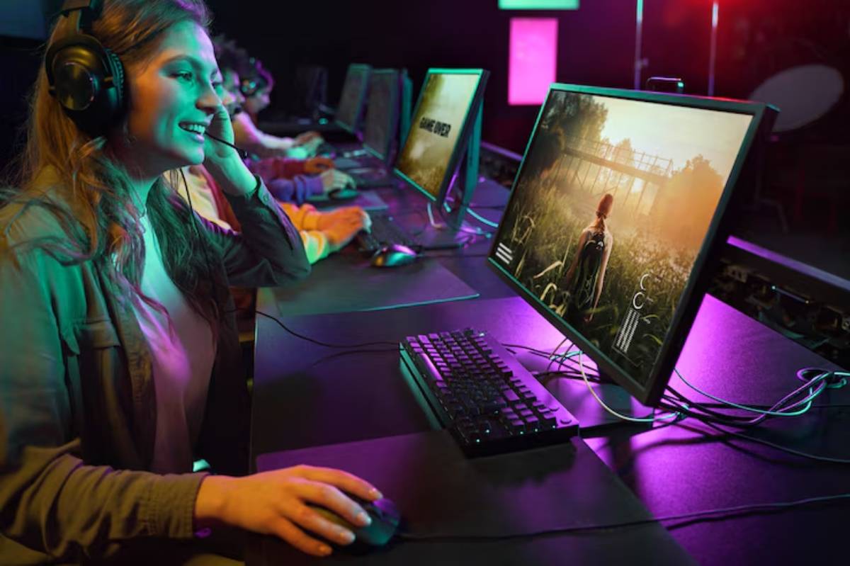 A gamer in headphones is focused on a computer screen displaying a lush, detailed scene, surrounded by colorful ambient lighting.