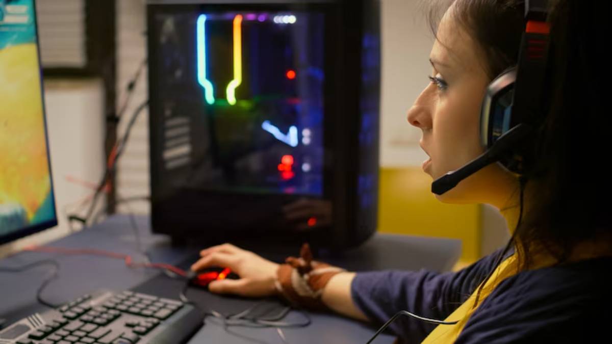 A close-up of a person gaming at a computer desk, using a mouse, with a colorful illuminated PC tower in the background.