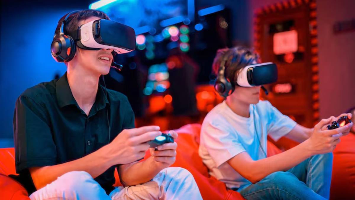 Two young gamers wearing VR headsets and headphones are seated on a red couch, engrossed in their virtual gaming experience.