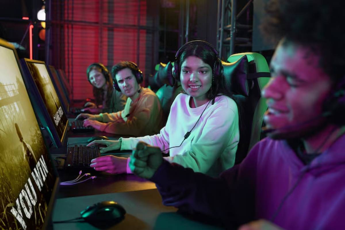 A group of gamers wearing headphones intensely focused on monitors displaying a game, illuminated by colorful ambient lighting.