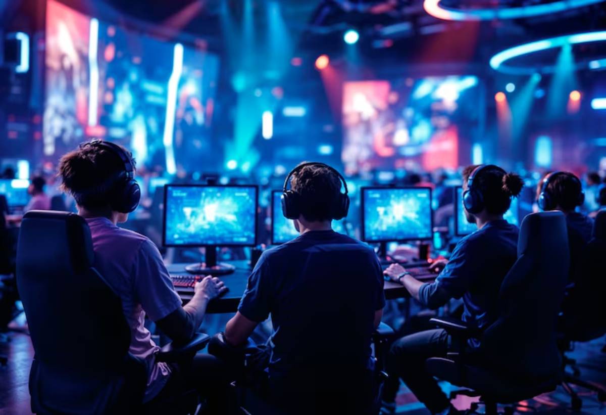 Four gamers in headphones intensely focus on their screens at an esports event, surrounded by vibrant stage lighting and large displays.