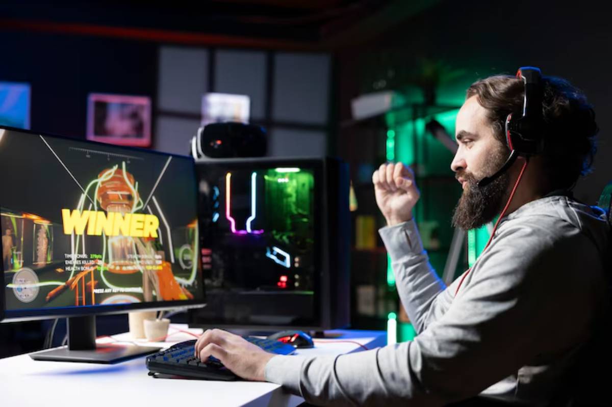 A gamer celebrates a victory with a raised fist, sitting at a desk with a colorful gaming PC and a monitor displaying 