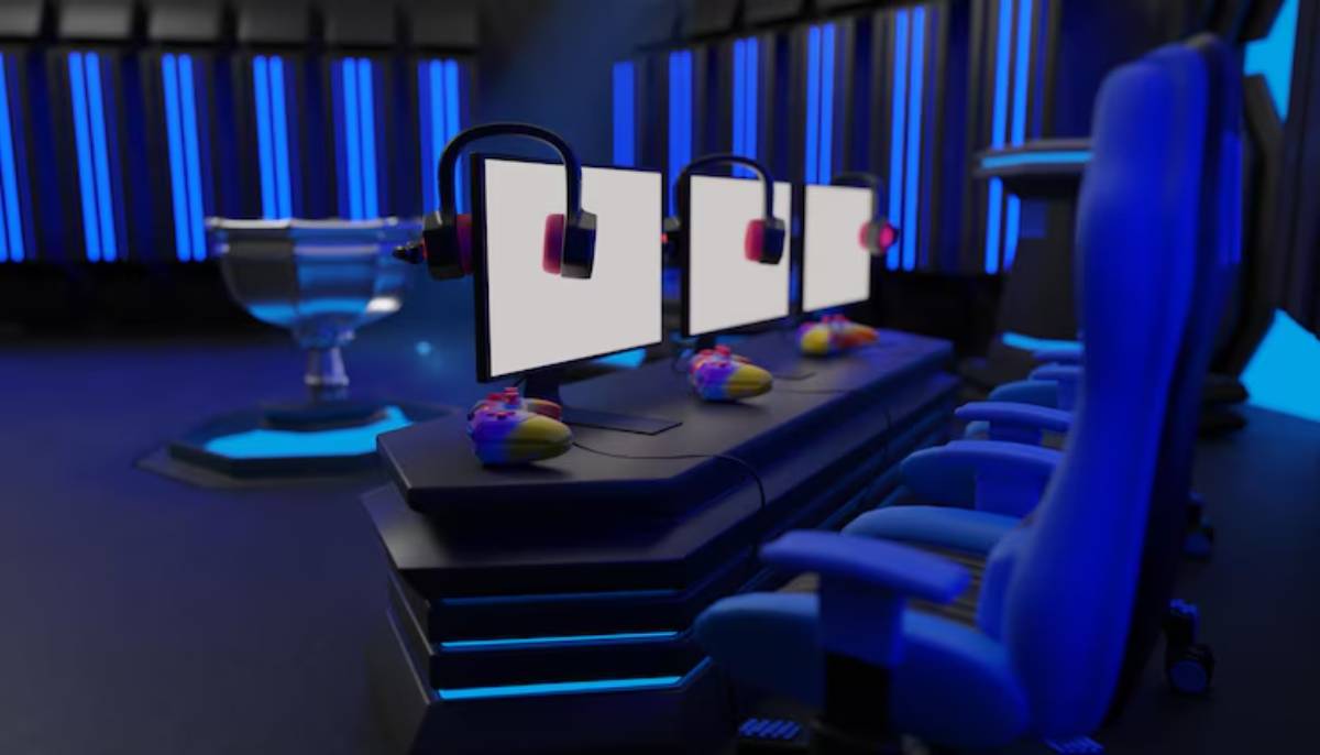 A gaming setup featuring three empty monitors with headsets, colorful controllers, and a trophy in a dimly lit room with blue lights.