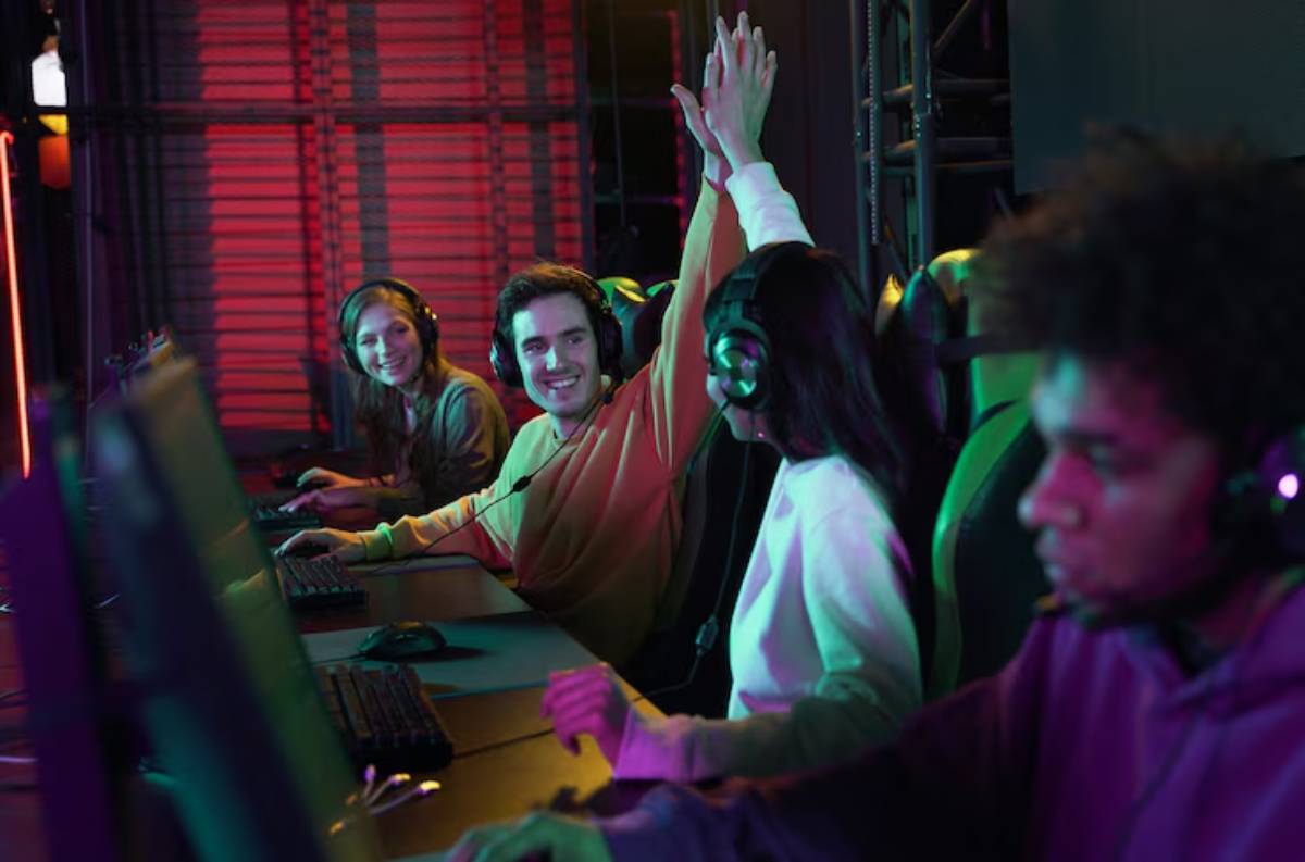 A group of gamers wearing headsets celebrates with raised hands in a vibrant, neon-lit gaming environment.