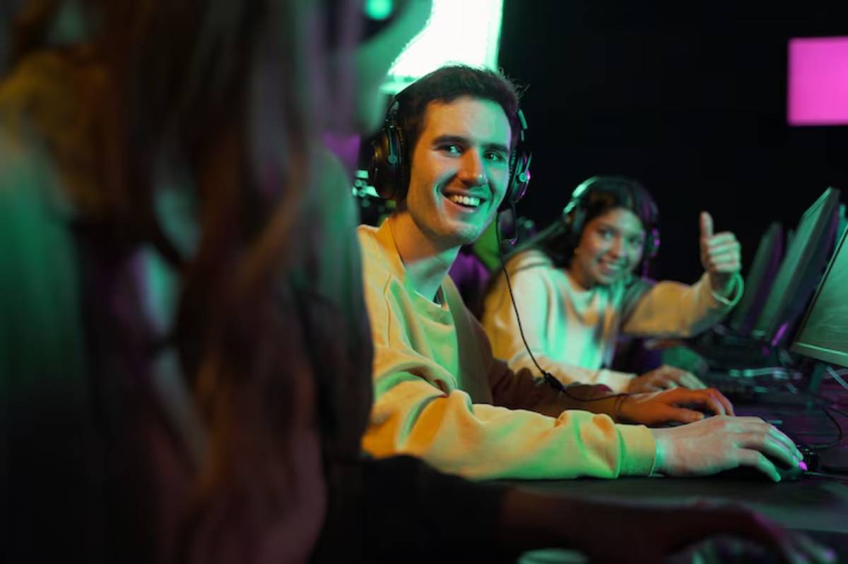 A group of gamers focused on their screens, wearing headphones, with colorful lights illuminating the gaming space.