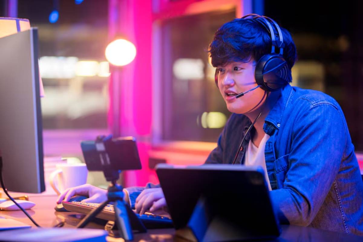 A person in a blue jacket and headphones types on a keyboard, illuminated by colorful lights in a cozy workspace.