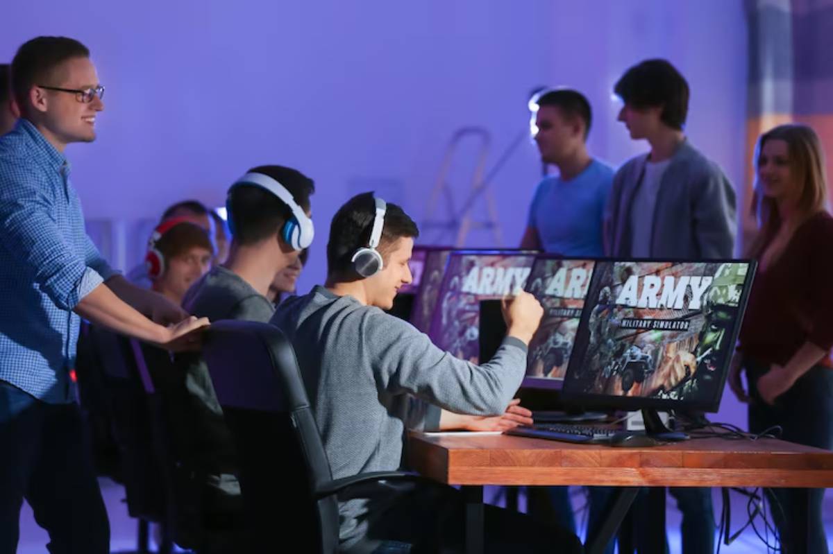 A group of gamers wearing headsets engages with computers displaying an Army military simulation game in a dimly lit room.